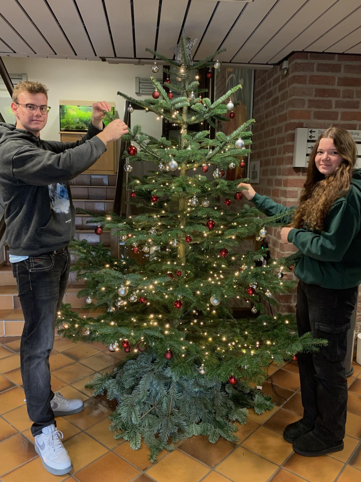 DIe beiden Auszubildenden vor dem geschmückten Tannenbaum